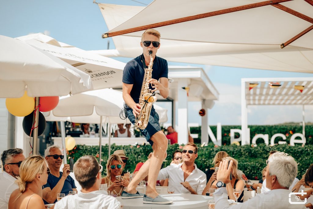 Saxofonista DeeSaxx hraje nad hosty na venkovní firemní párty