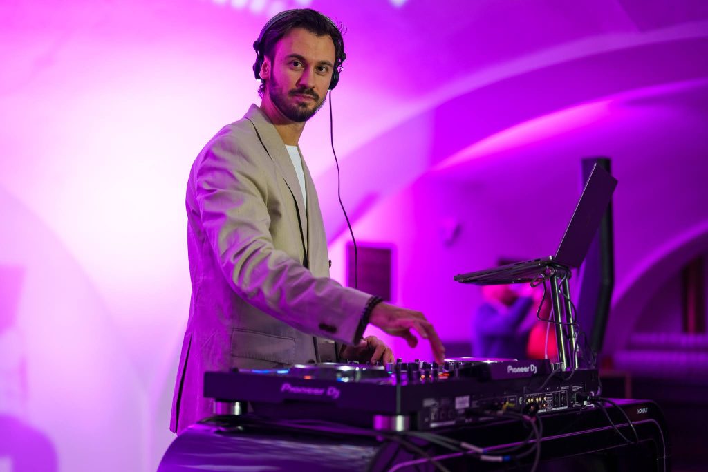 DJ Bury mixing behind the decks at a corporate party in a purple-lit hall