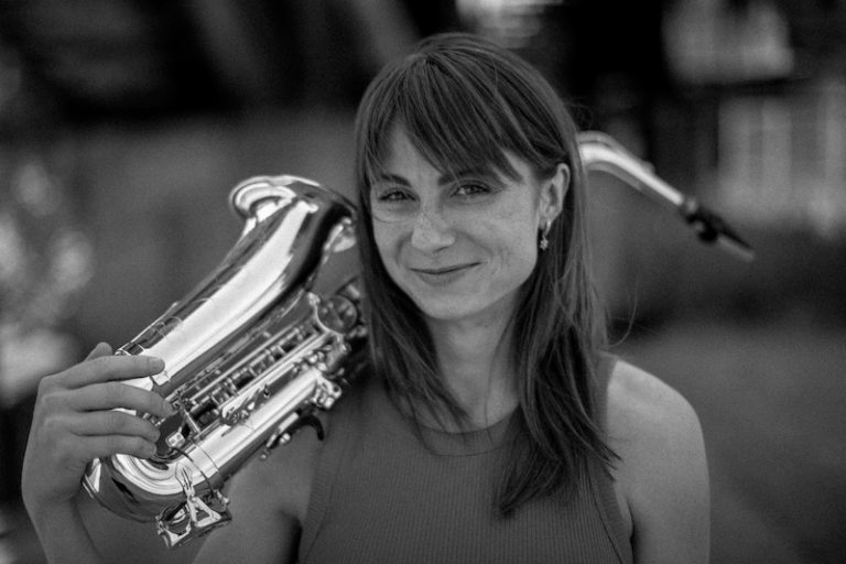 Black-and-white promo portrait of saxophonist Nikisaxi with her saxophone, BURYSAX