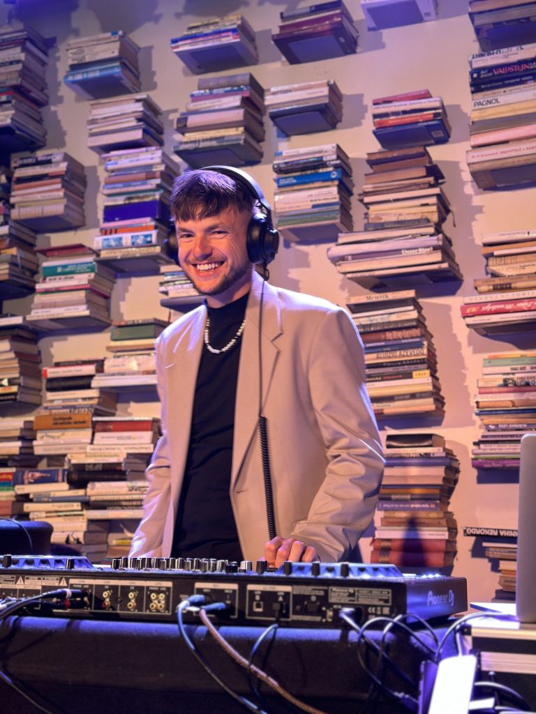 Smiling DJ and host Václav Brom behind the decks in front of a wall of books – DJ for corporate events in Prague