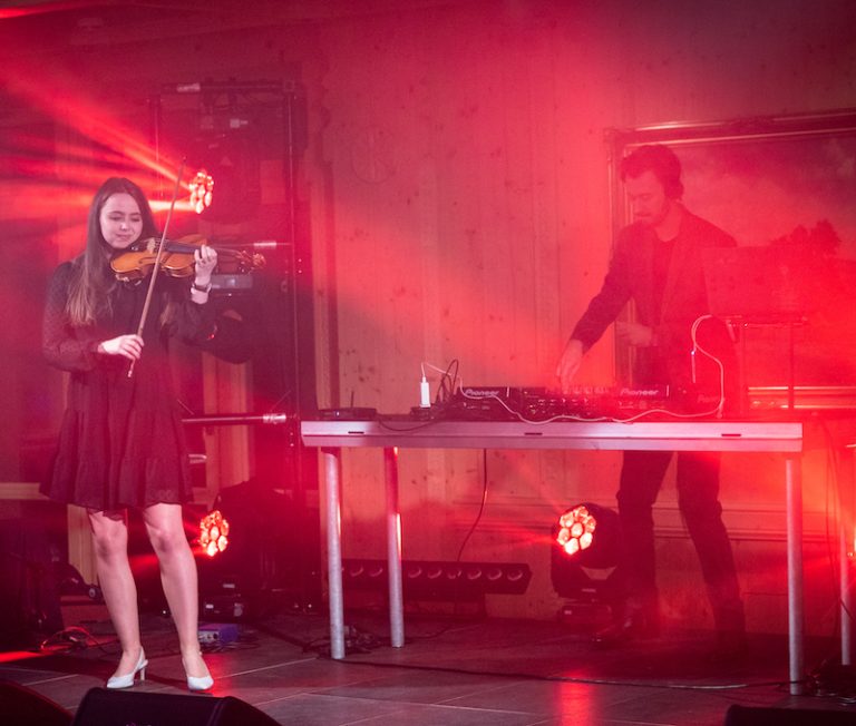 Violinist Alžběta Králová performing with a DJ on stage in red light at a corporate party
