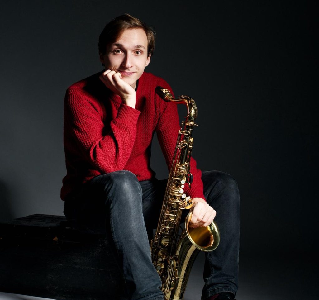 Saxophonist Kryštof Janáček in a red sweater with an alto saxophone – saxophonist for corporate events in Prague