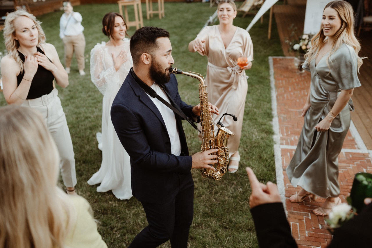 Saxofonista hraje mezi svatebními hosty na zahradě fary Brixi