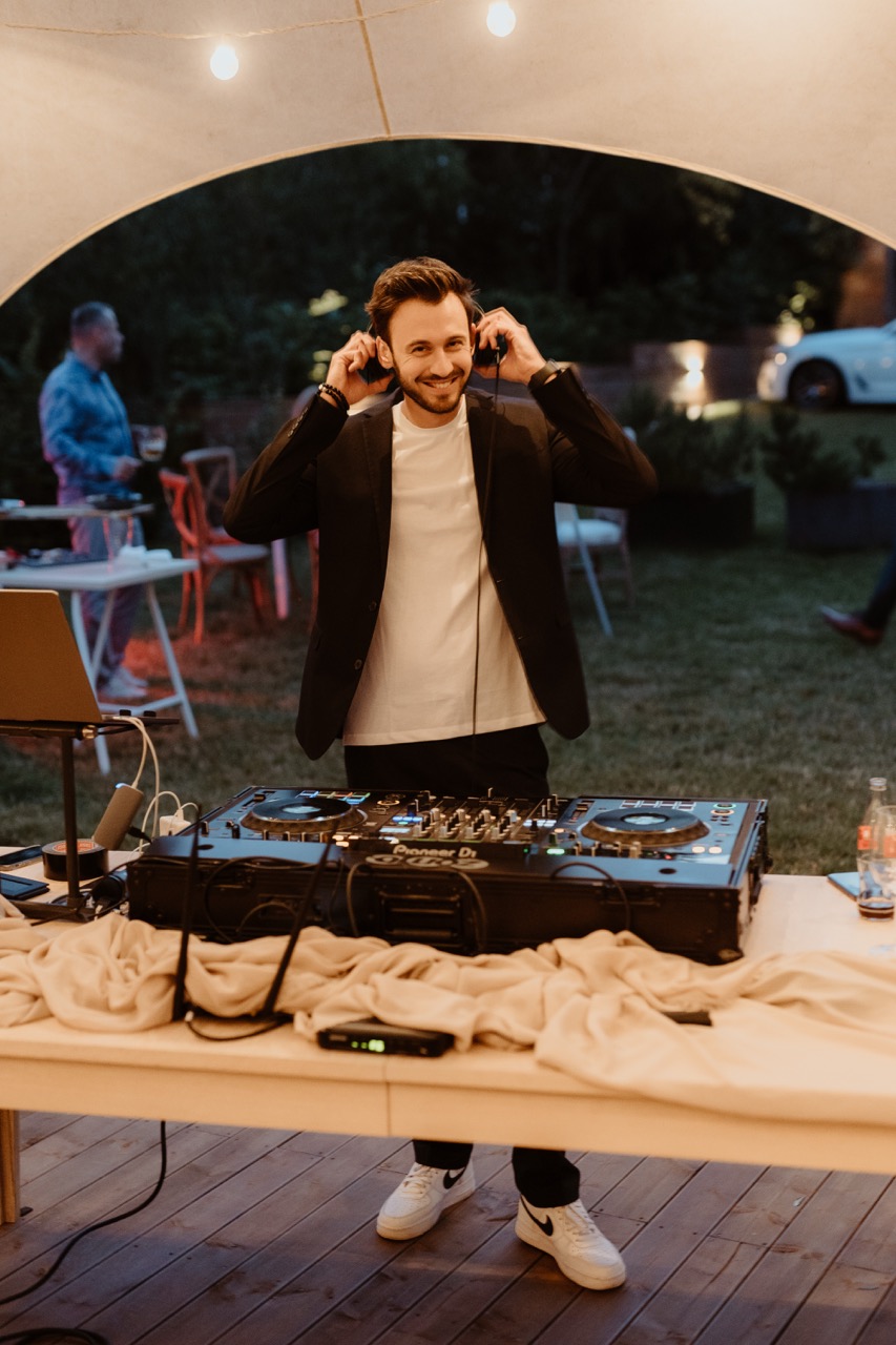 DJ se sluchátky za DJ pultem pod svatebním stanem na faře Brixi