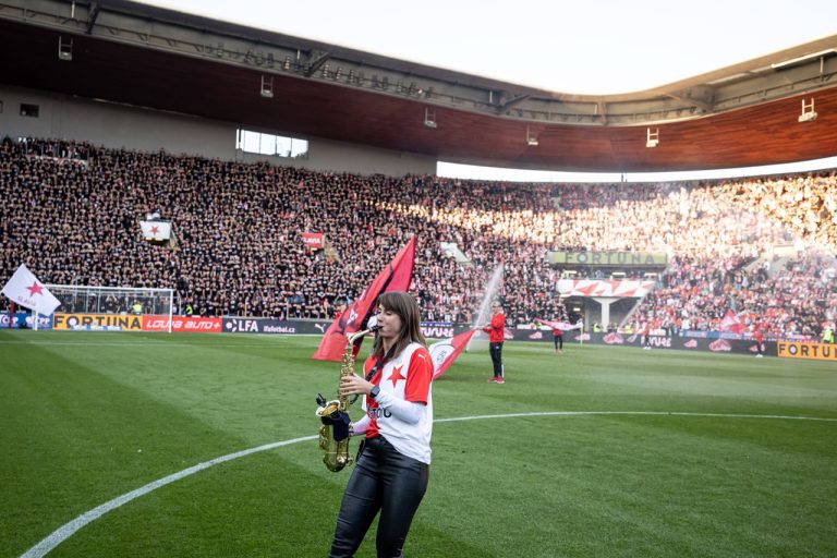 Saxofonistka Nikisaxi hraje u středového kruhu Eden Areny během předzápasové show derby Slavia–Sparta, za ní houslistka Iska.muse a vlajkonoši