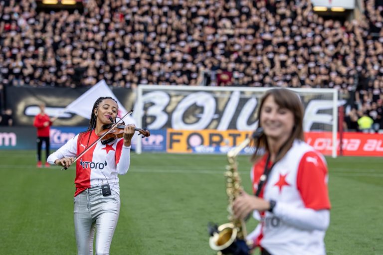 Houslistka Iska.muse a saxofonistka Nikisaxi hrají před kotlem slávistických fanoušků s transparentem Bojujeme při derby Slavia–Sparta