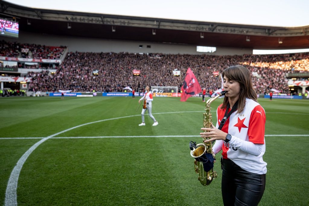 Saxofonistka Nikisaxi hraje na saxofon na trávníku Eden Areny před derby Slavia–Sparta, v pozadí houslistka Iska.muse a zaplněné tribuny