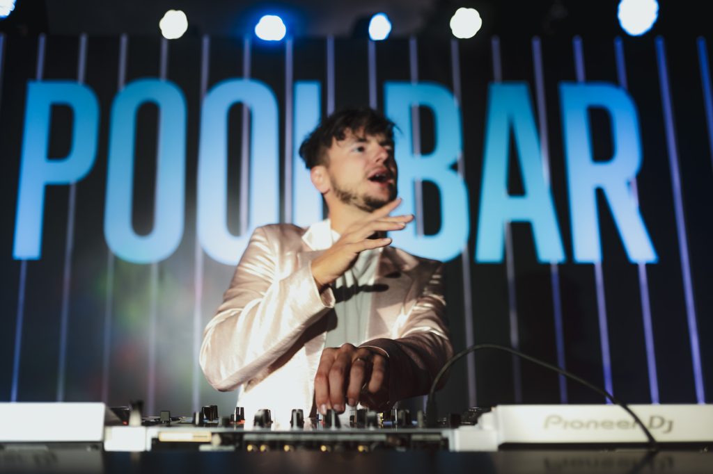 DJ Václav Brom za DJ pultem s nápisem Pool Bar, party Accolade KVIFF 2022